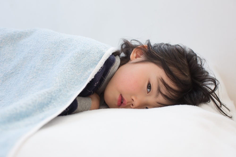 little girl lying in bed under covers