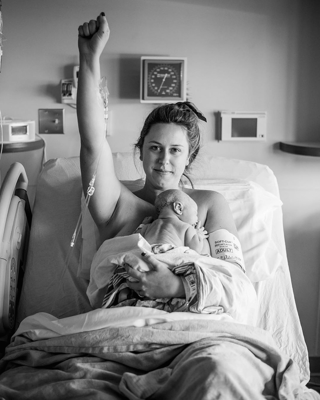 woman raising her first while holding her newborn after giving birth