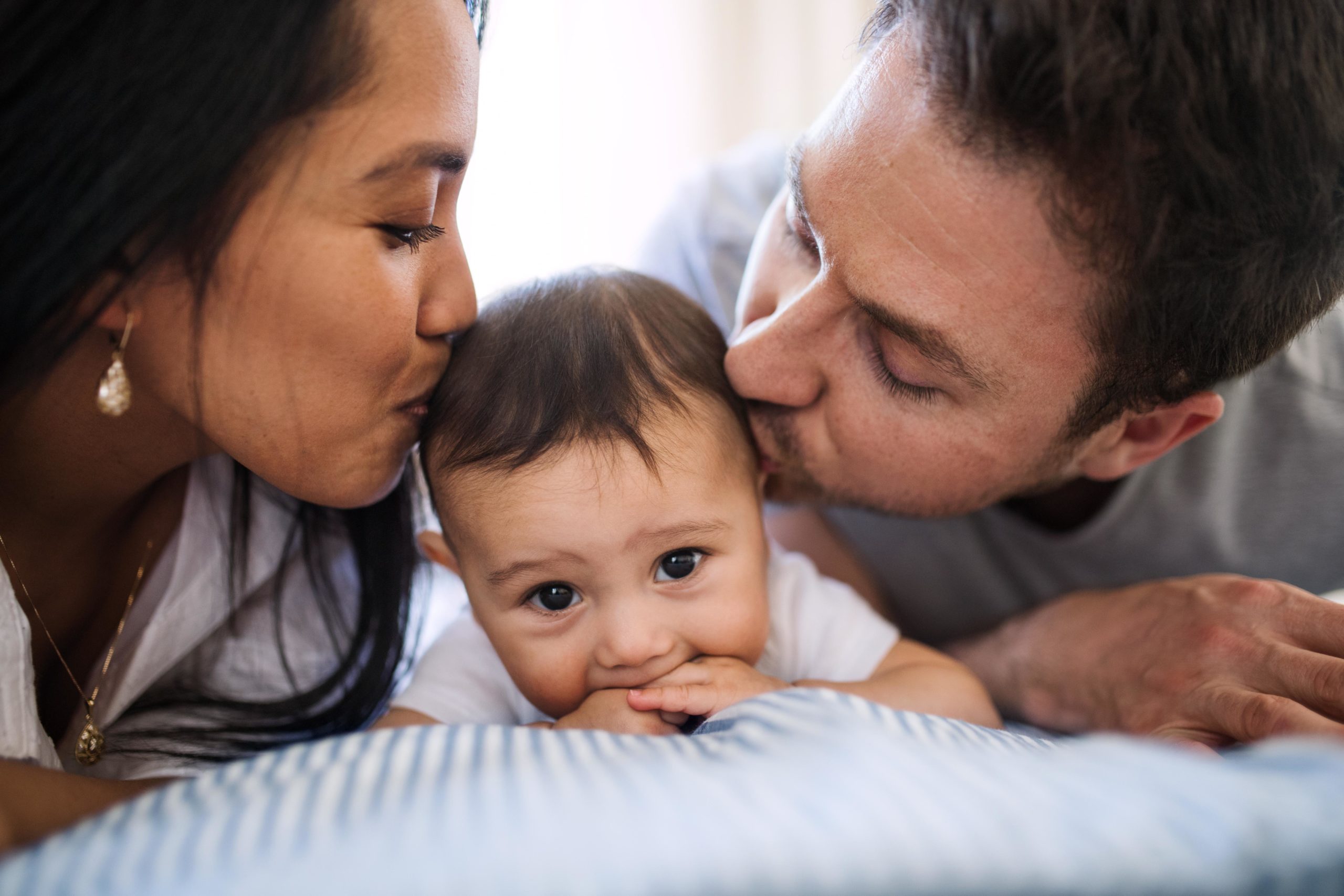 two parents kissing each side of a baby's head