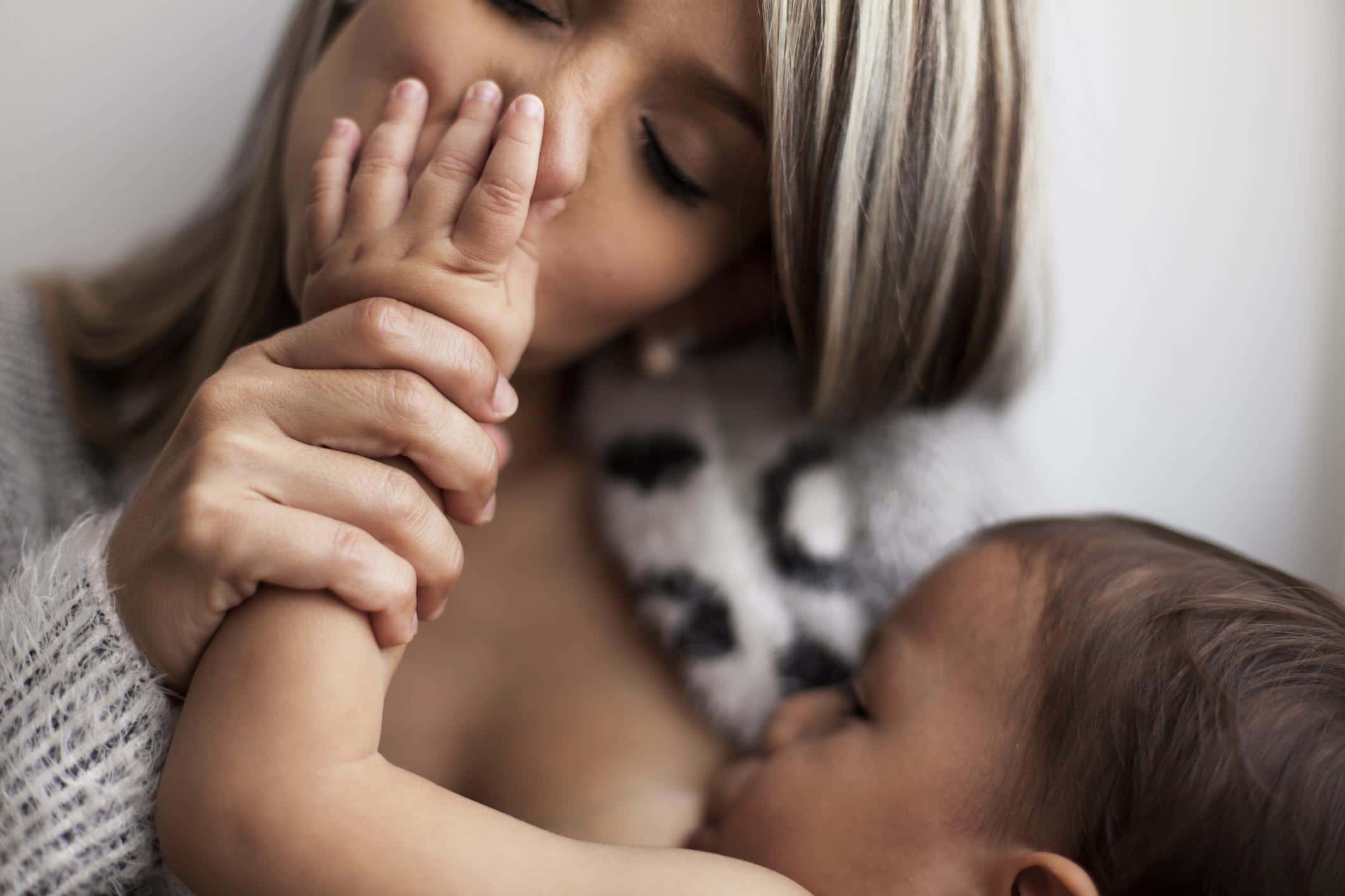 mom kissing baby's hands while breastfeeding