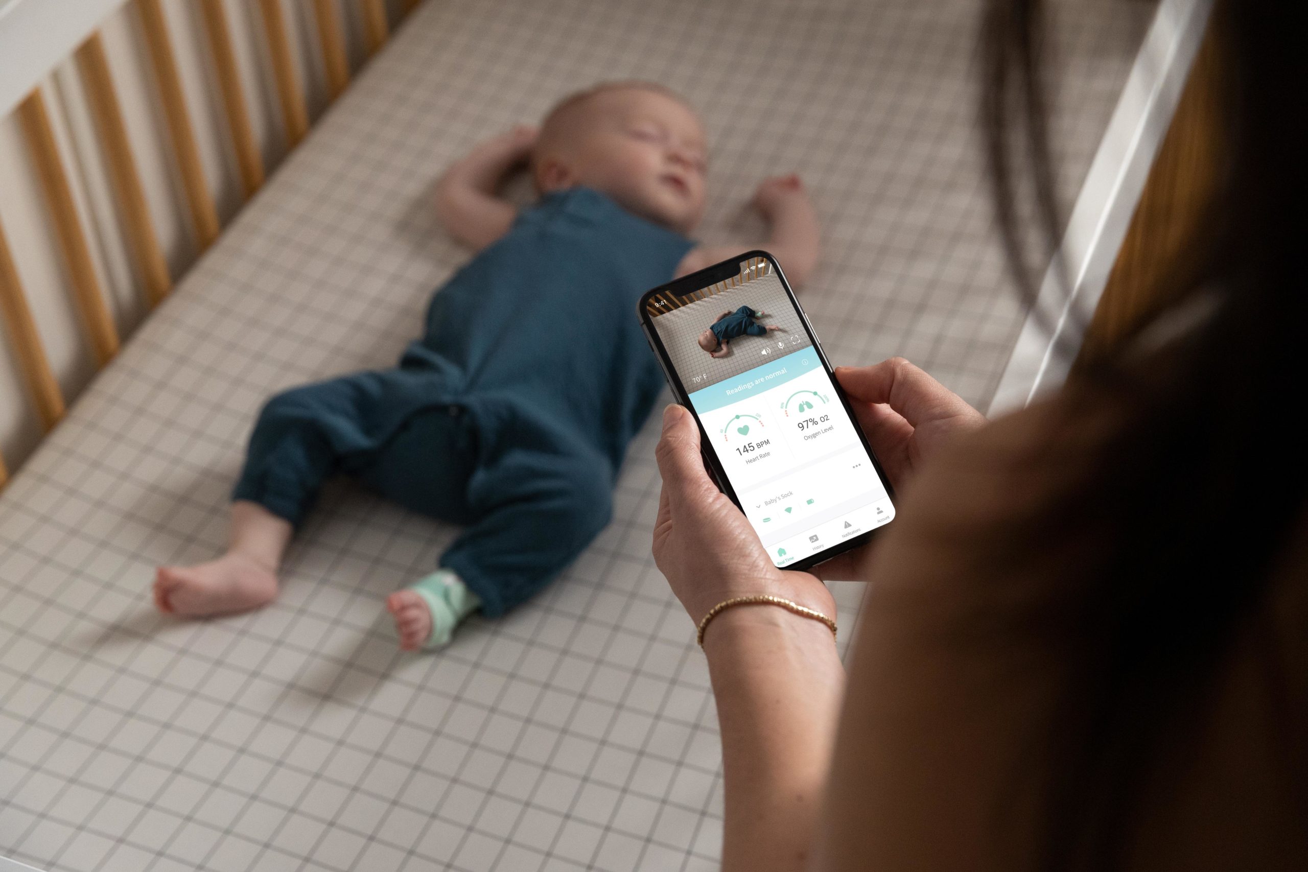 mom looking at newborn baby sleeping through the Owlet app