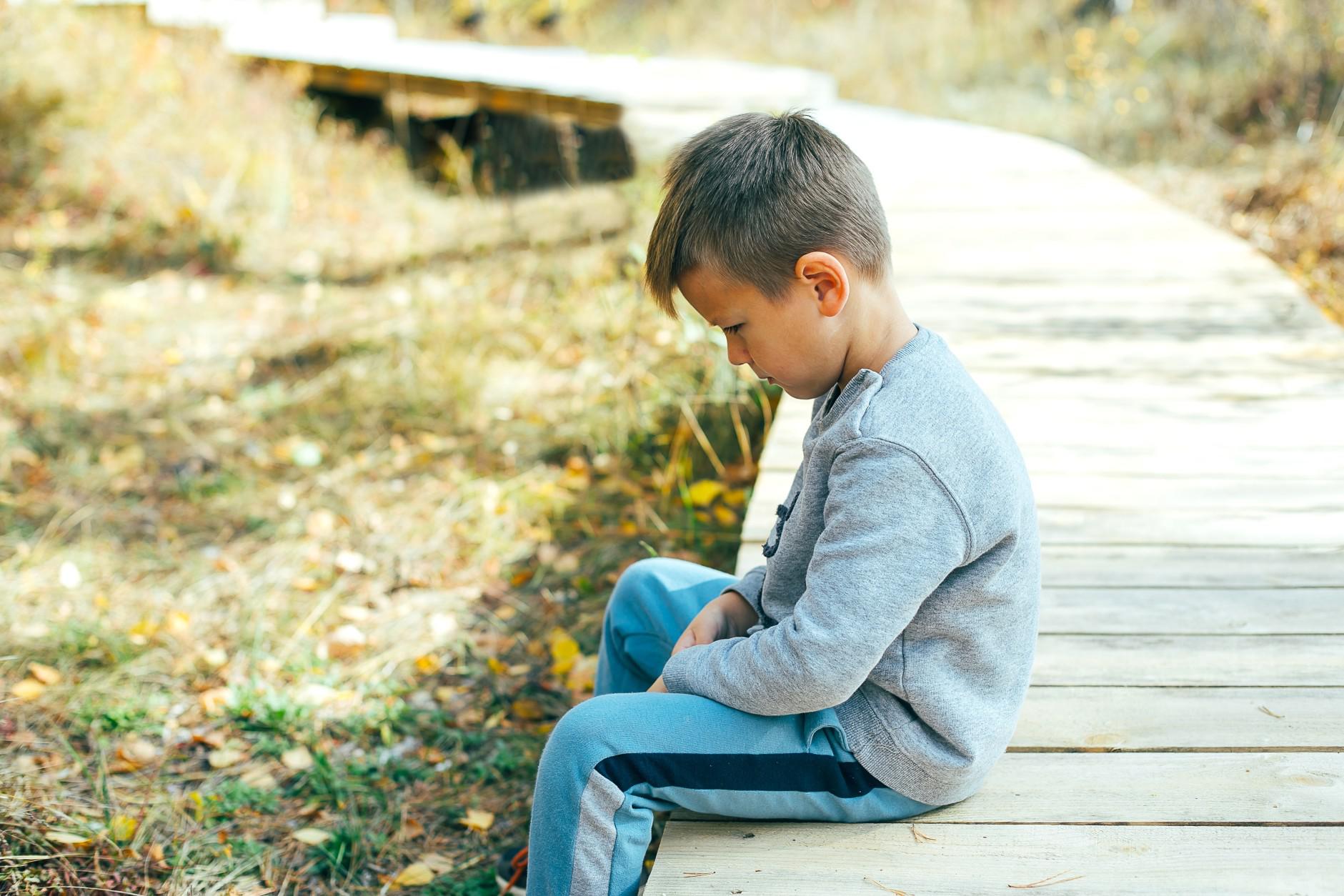 sad little boy sitting on a bridge - Motherly's tips for dealing with school bullying