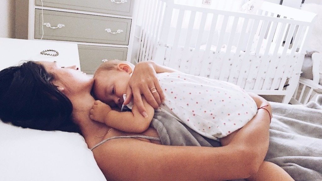 mom holding baby against her chest lying down in a bed