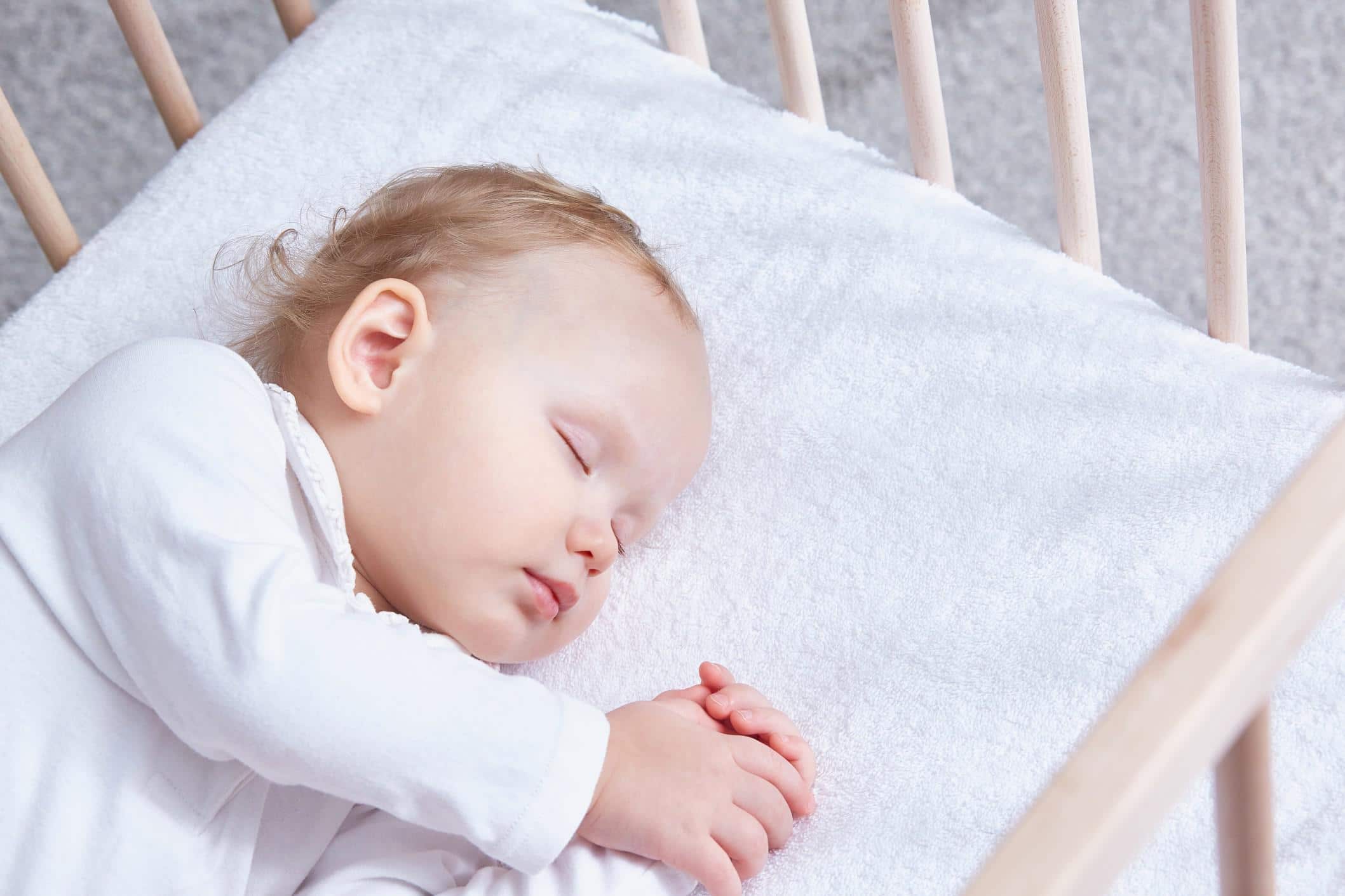 12-month-old baby sleeping in a crib with its hands together
