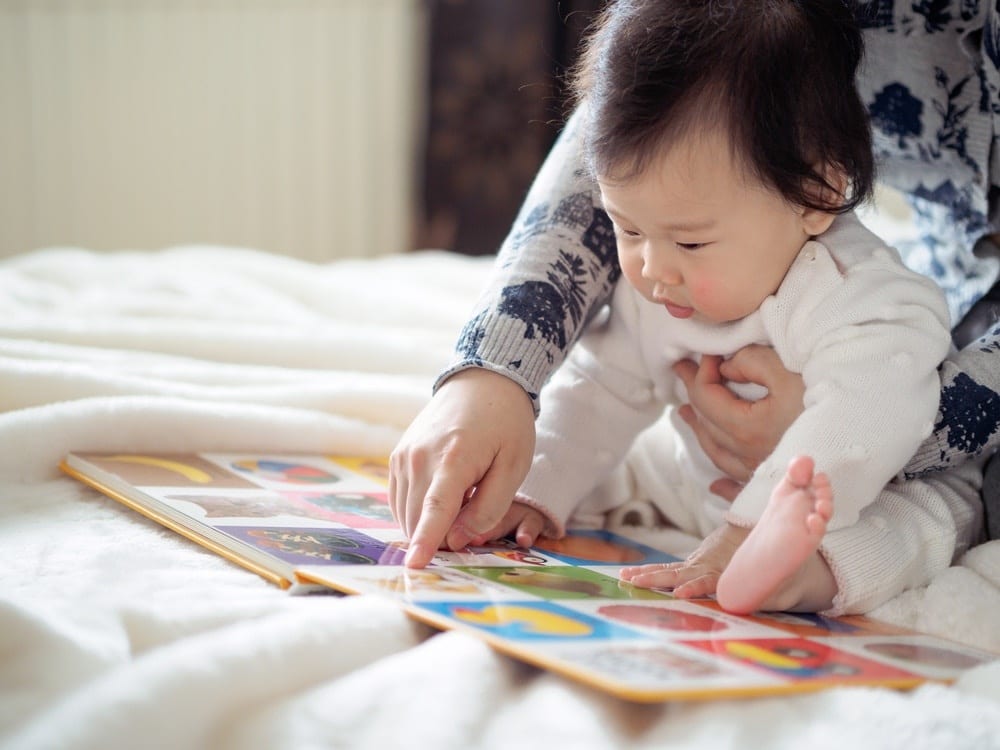 mom pointing out a picture in a book to her baby, wondering when to start reading to baby
