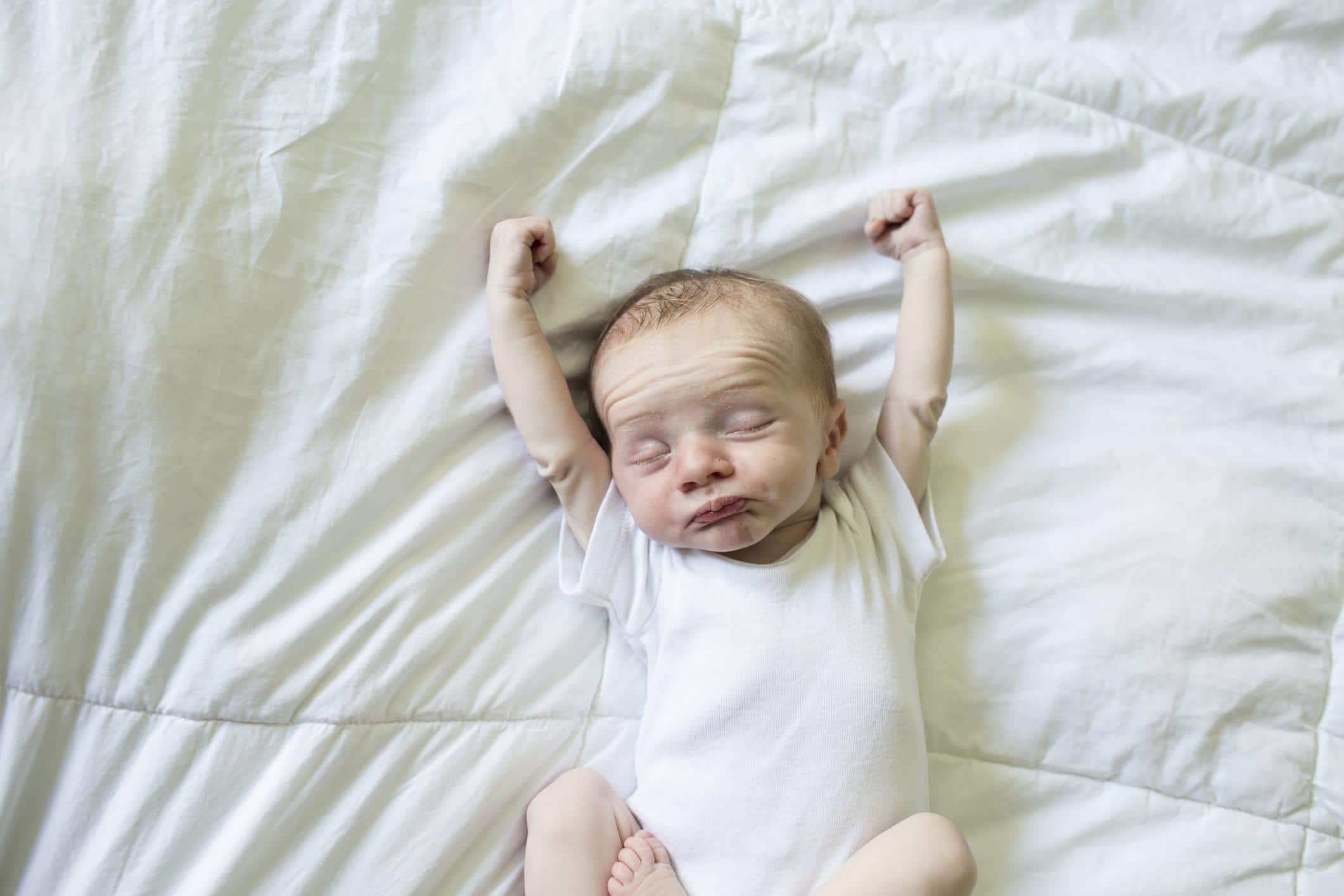 one-week-old baby stretching on a bed