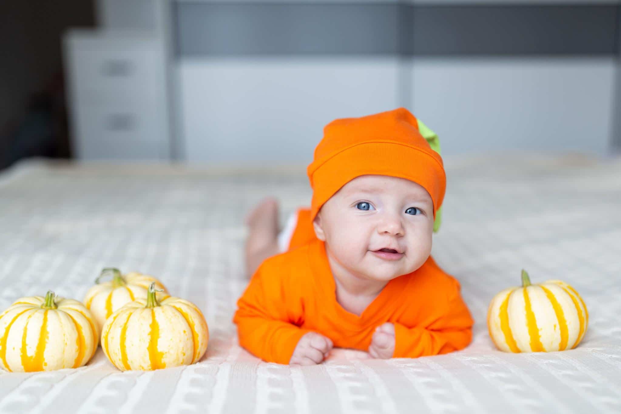 baby dressed up like a pumpkin laying beside baby pumpkins - october baby names