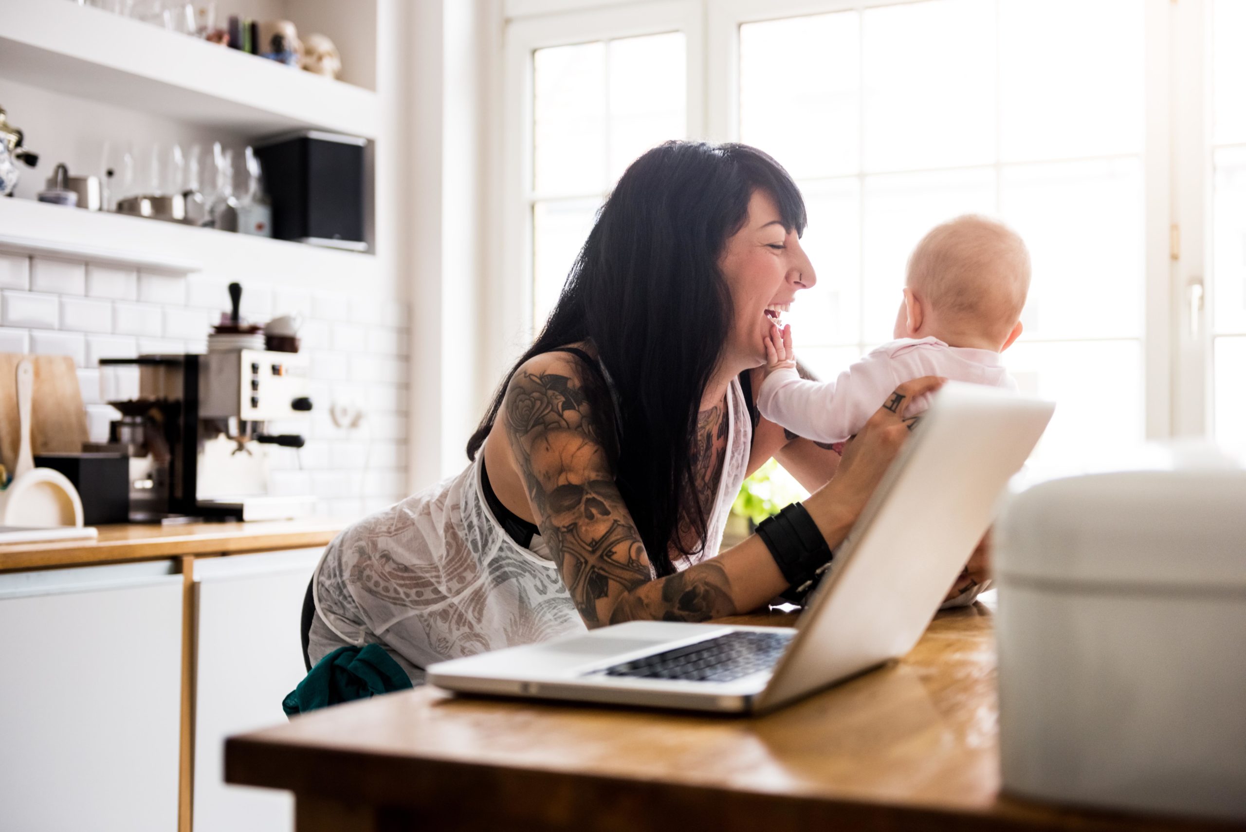 mom laughing and telling a mom jokewhile holding baby on the counter