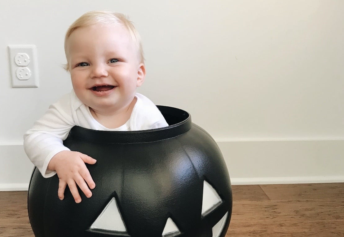 baby sitting in a plastic pumpkin, celebrating its first halloween