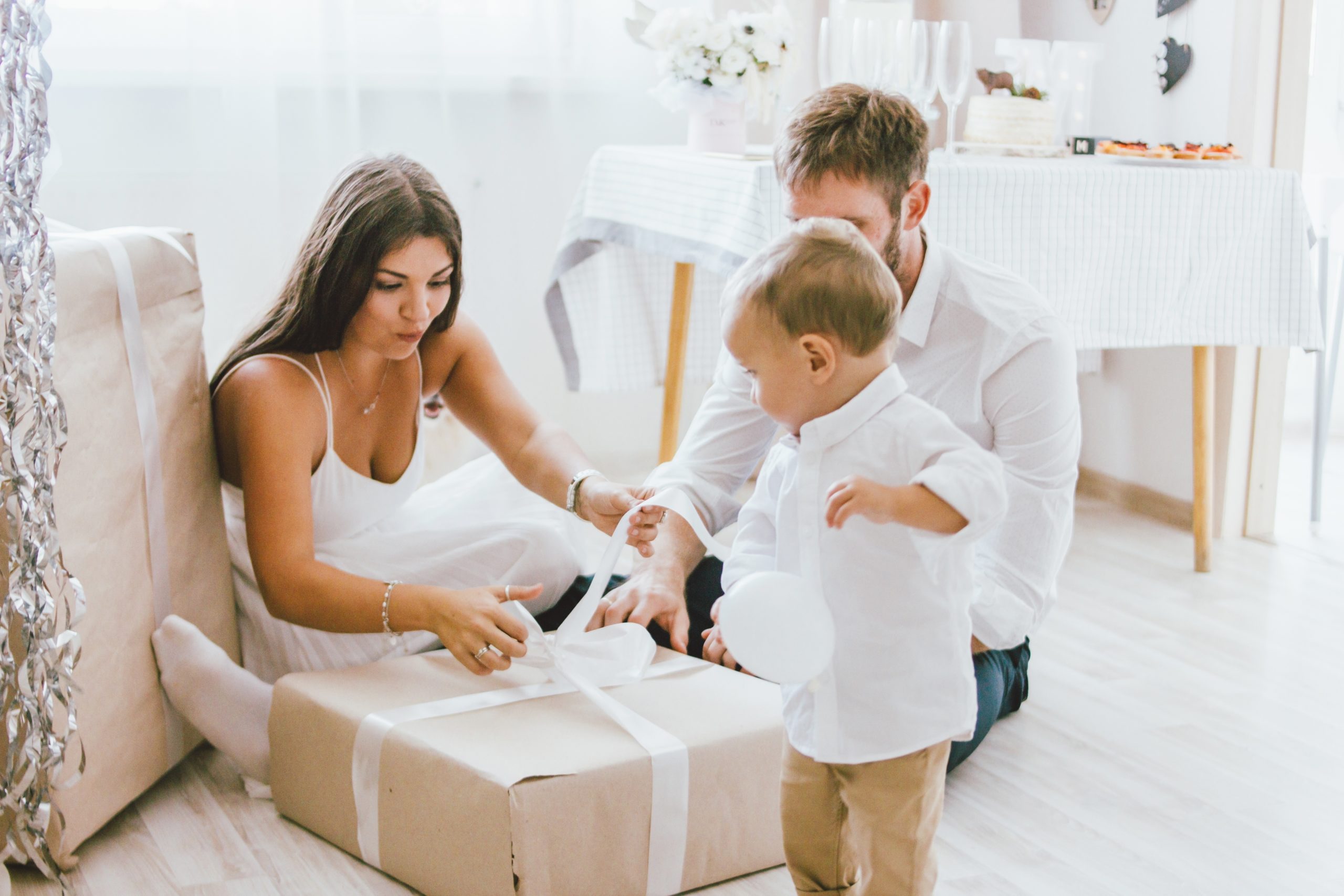 mother, father and child folding ribbon over a gift- holiday stress