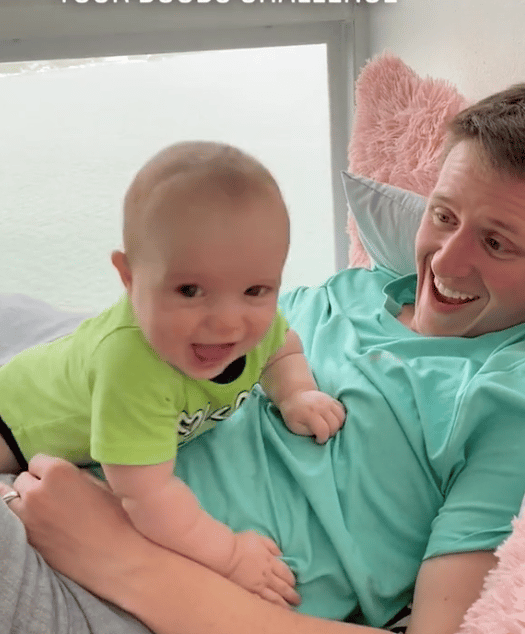 dad laughing with newborn baby climbing on him