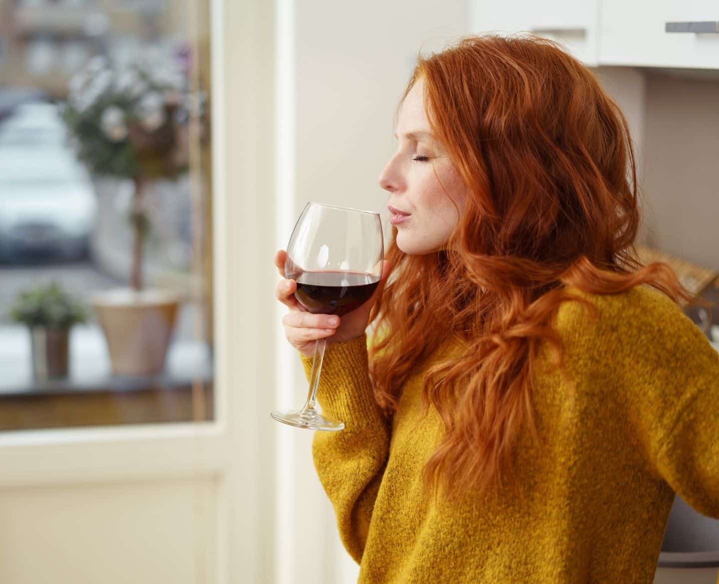 woman nursing a glass of wine in yellow sweater