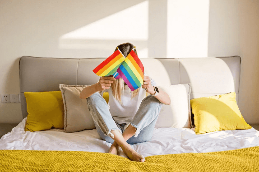 woman sitting on a bed holding pride flags