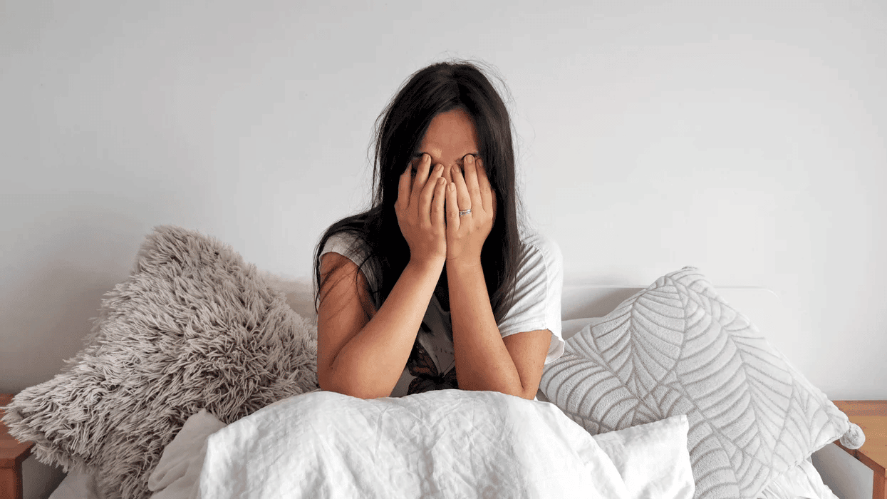 tired woman holding hands over face laying in bed-self-care during the holidays