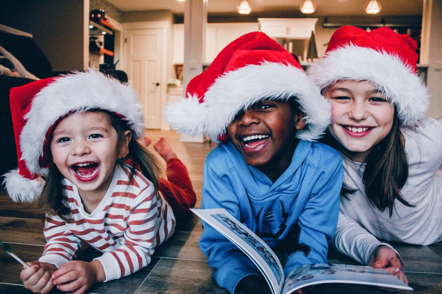 3 kids wearing santa hats and reading christmas books- christmas books for kids