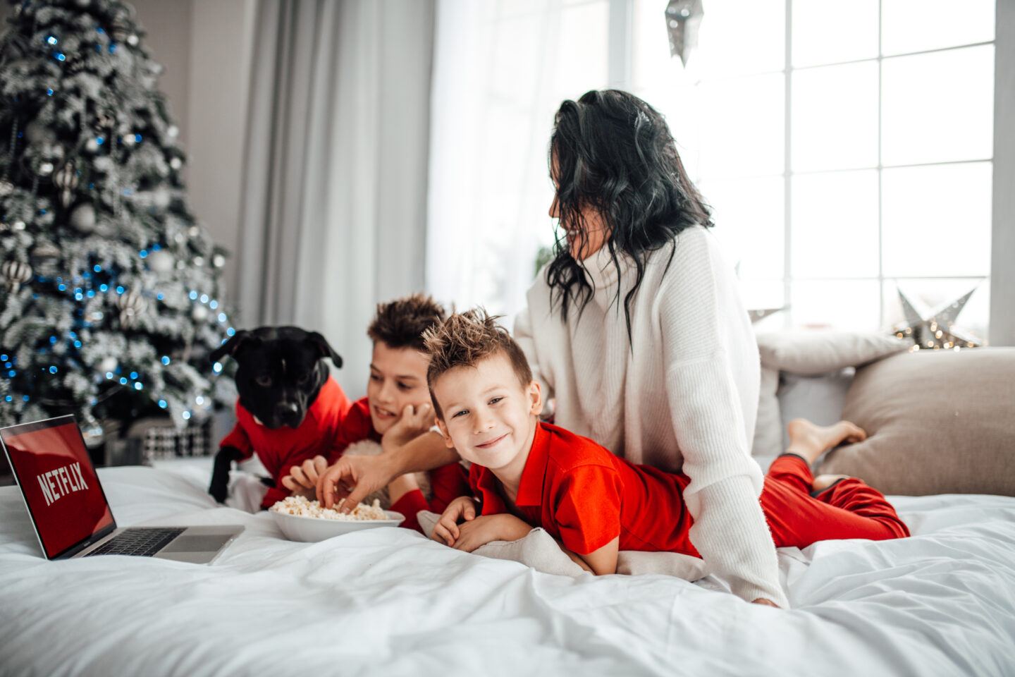 mom and kids and dog laying by christmas tree eating popcorn christmas movies for kids