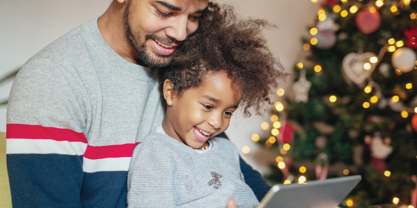 father and daughter looking at a tablet by the christmas tree - norad santa tracker