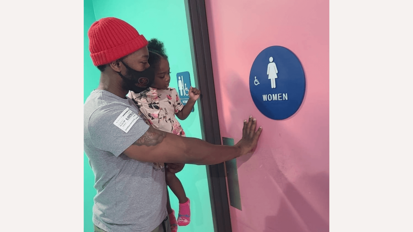 Dad holding baby girl in front of a women's bathroom