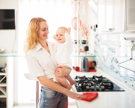 caucasian mom with baby in her arms cleans the kitchen in the house mother restores order wipes the t20 ZYvynR Motherly