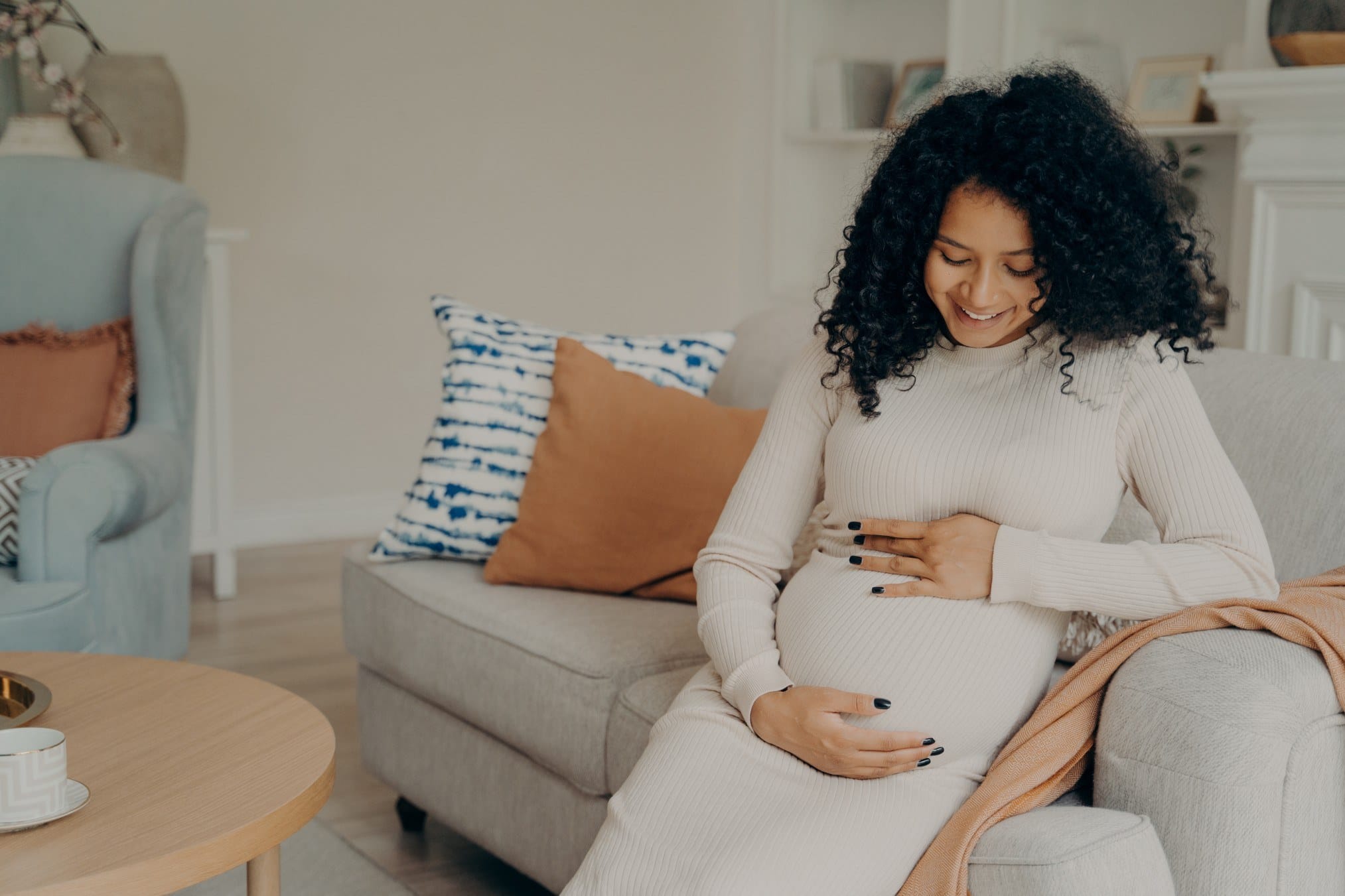 happy young pregnant afro american lady in white dress with long curly hair looking at her belly with t20 2KlAR8