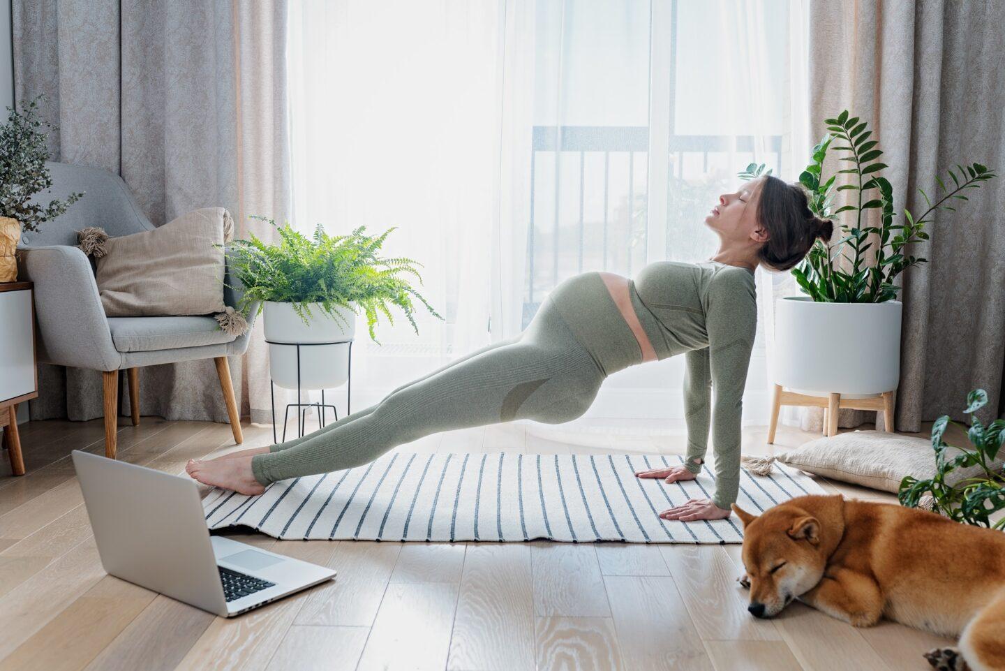 Pregnant woman exercising in living room with laptop open