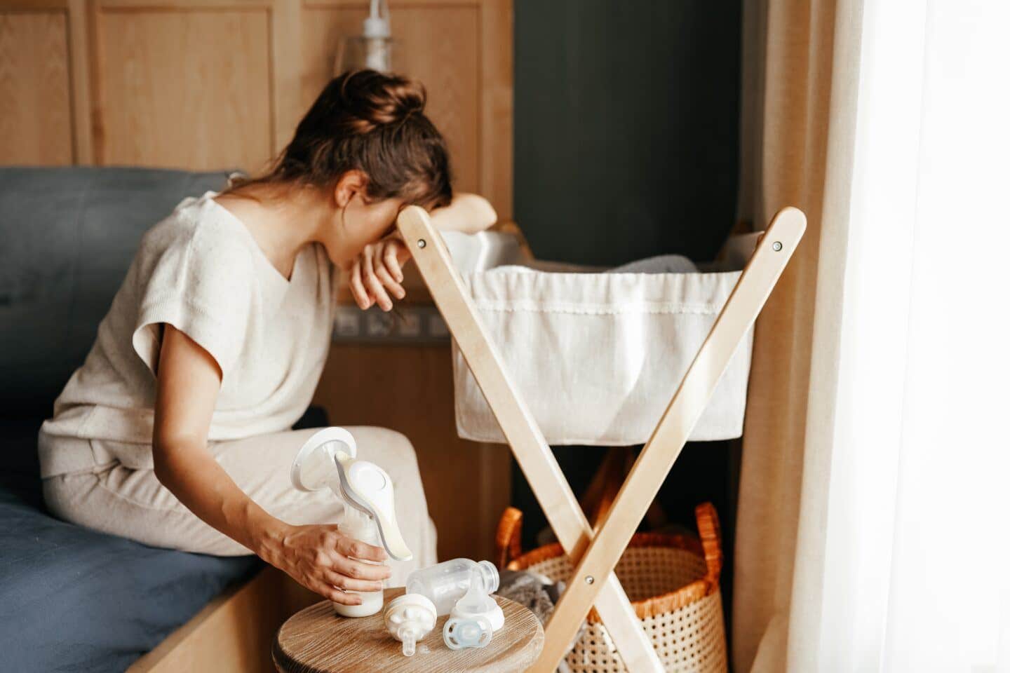 mother pumping by baby's bassinet looking down with head on hand