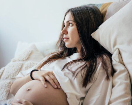 titovailona via Twenty20 close up portrait of attractive pregnant young brunette woman lying on the bed and gently touching t20 RJGyrm