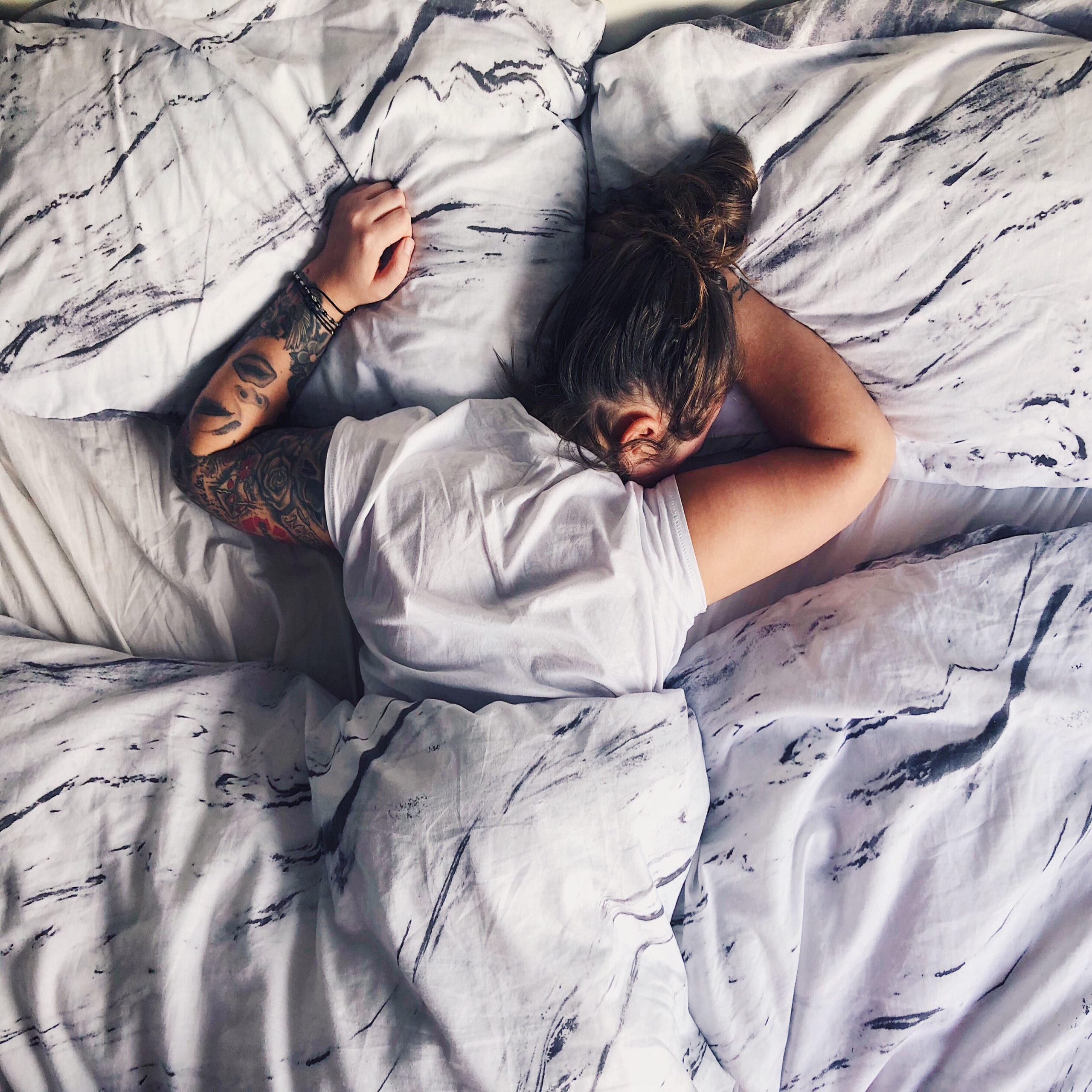 woman sleeping on stomach in bed with tattoos on arm