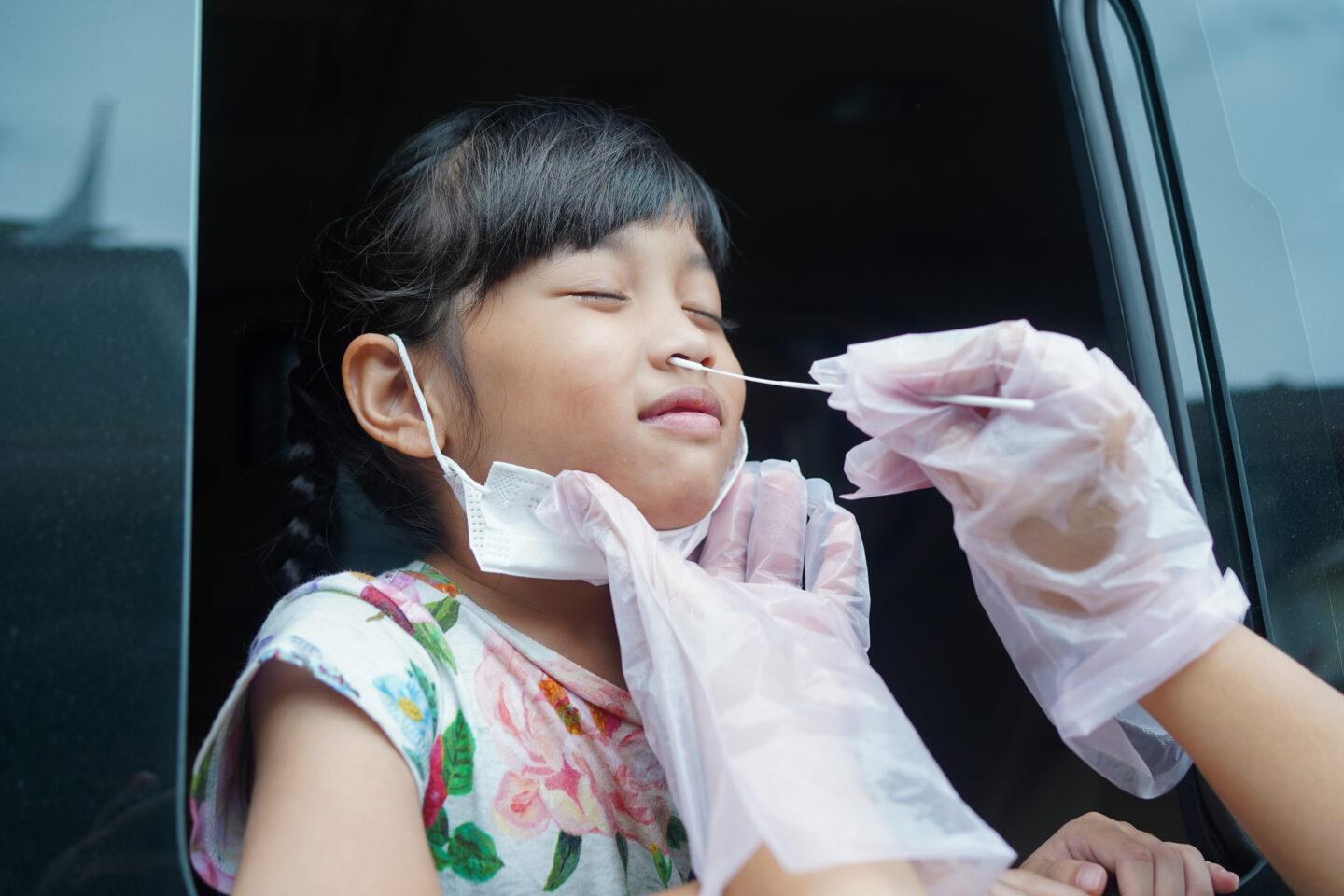 covid and diabetes in kids: young girl having covid PCR test done through car window