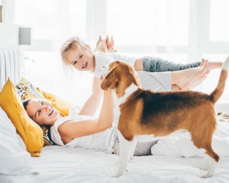 growth mindset in mothers: mother holds baby up on knees while lying on bed next to dog