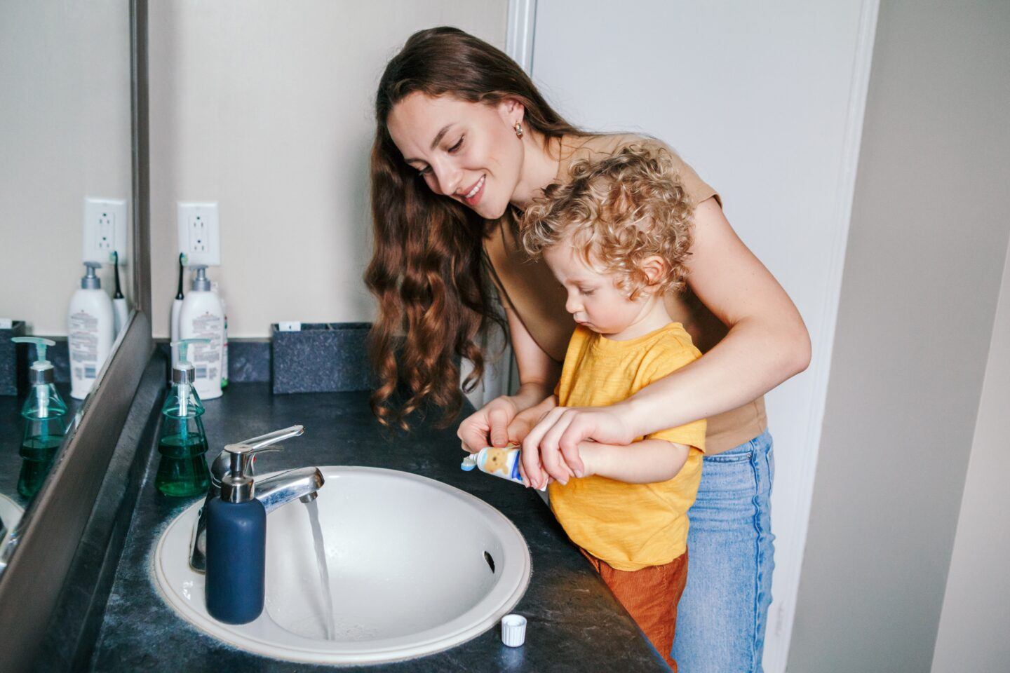 Toddler fights tooth brushing: mother helping toddler brush teeth at bathroom sink
