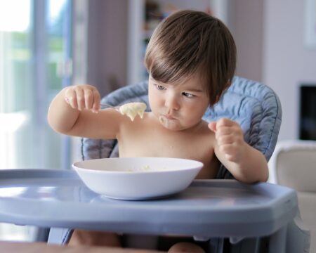 funny little baby boy eating porridge looking at full spoon in his hand sitting in high chair child t20 kRGpnp Motherly