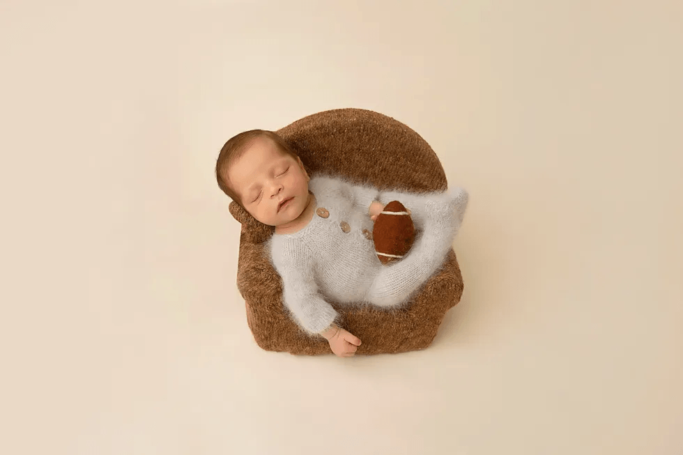 newborn baby laying on a chair holding a football, one of motherly's favorite newborn pictures