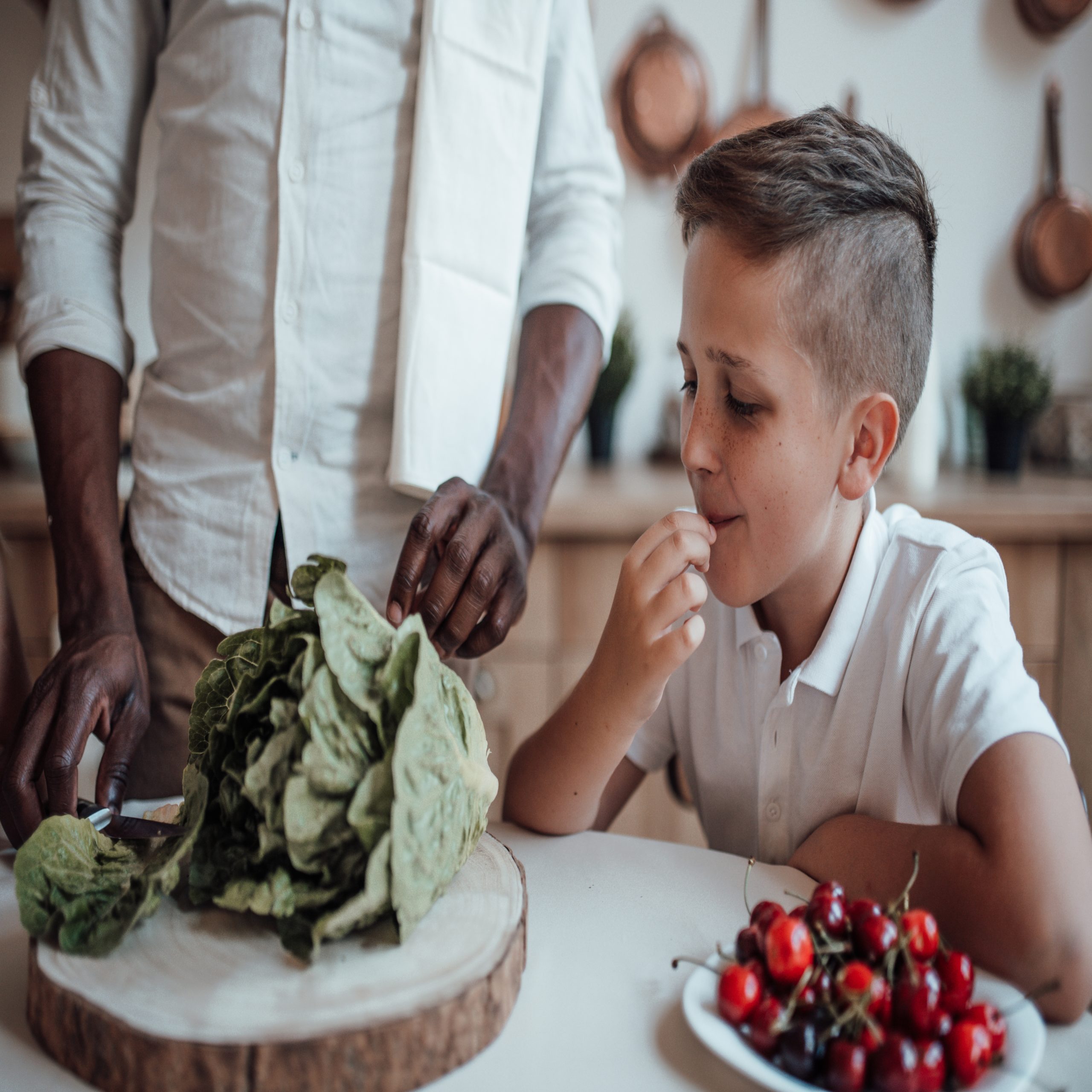 Kids' mental health tied to fruit and veggie intake, young boy at table with family tasting lettuce and cherries