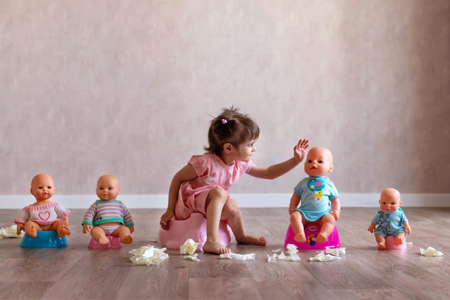 Beautiful smiling little baby sitting on potty. Cute adorable funny child girl using chamber pot together with her baby doll. Toilet training concept. Toddler learning to use the Toilet.