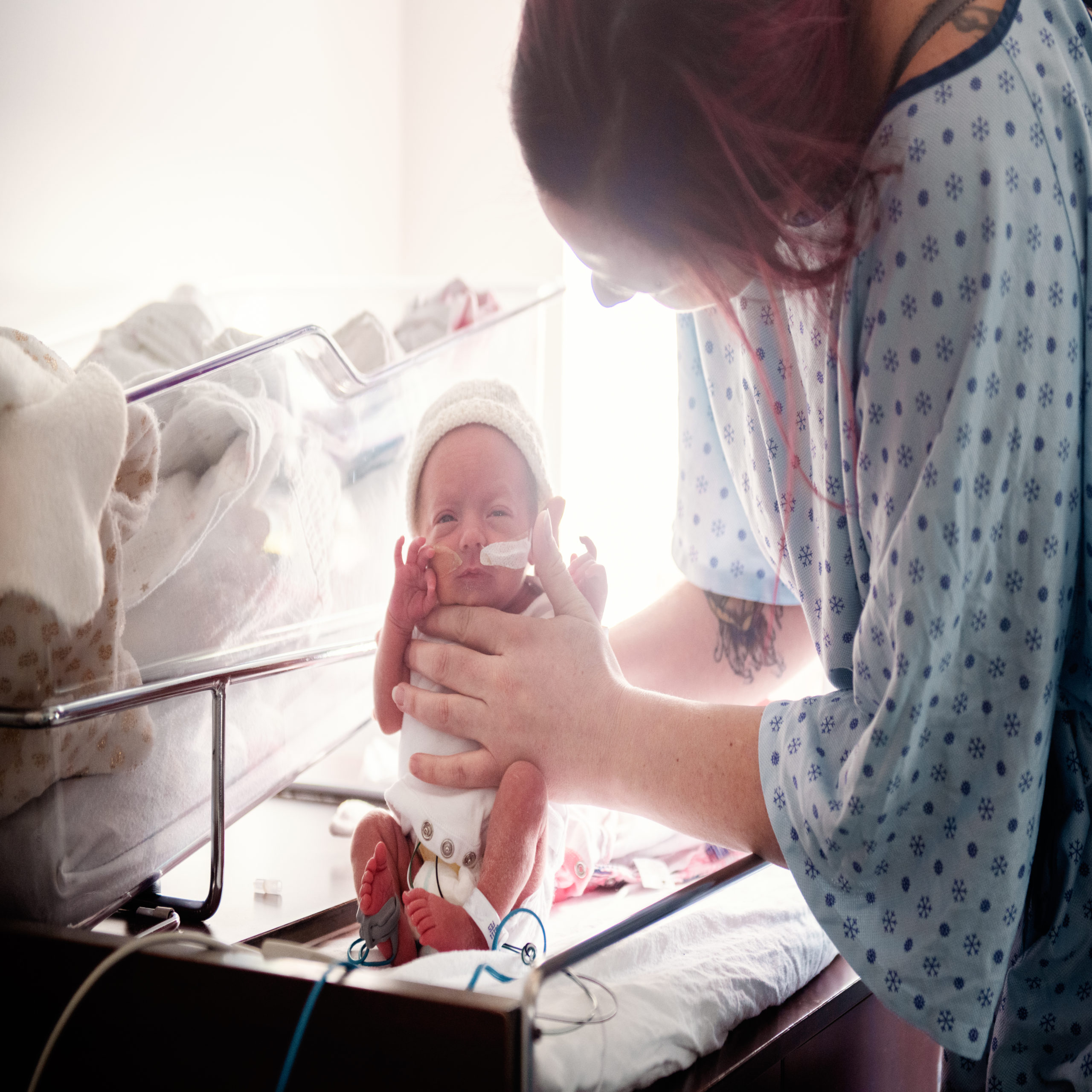 Mother holding baby in hospital isolette, preparing to bring baby home from nicu