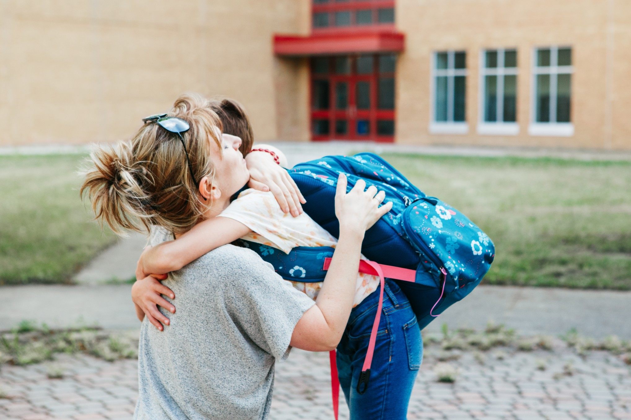 happy caucasian mother parent kissing embracing girl child kid on school yard and saying goodbye back t20 vOLXAv