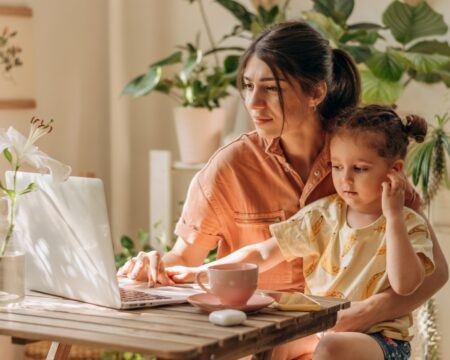 a young mixed race mother working at a laptop her three year old daughter is sitting on her t20 JJ2rgO Motherly