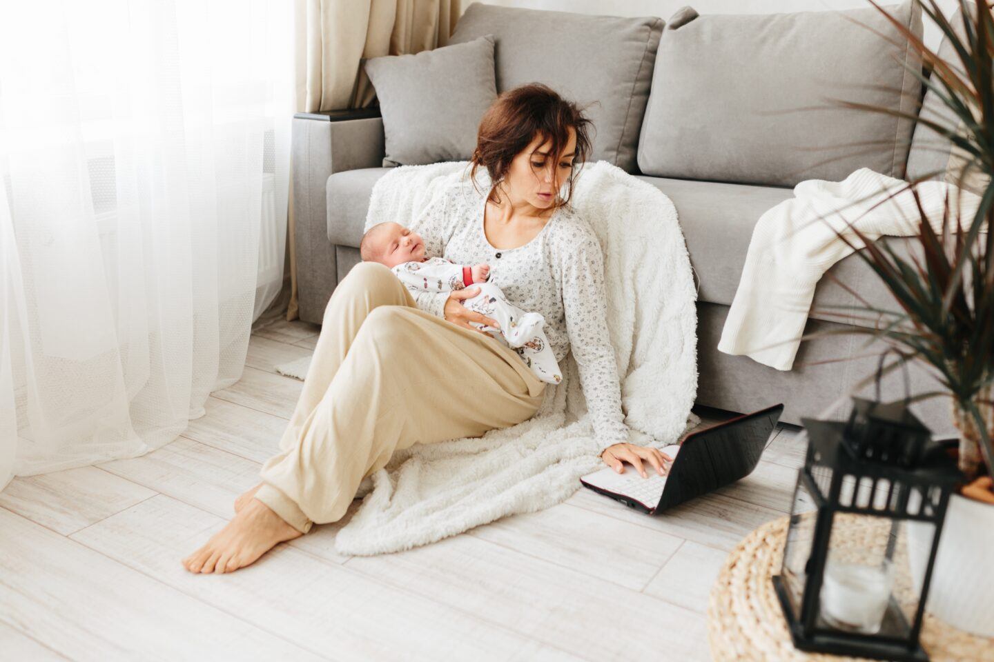 Mother holding a sleeping baby and working on a laptop