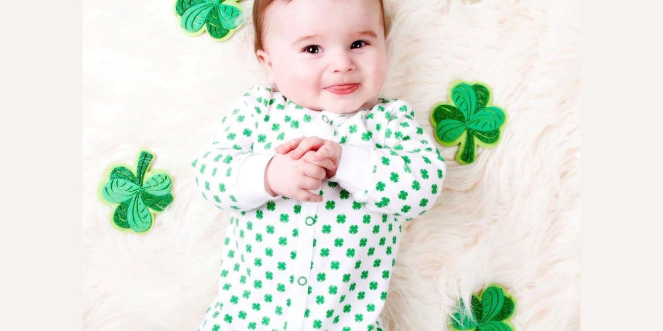 smiling baby laying down on a white blanket wearing a shamrock onesie-irish baby names