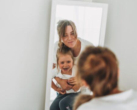 young mother and daughter in white t shirts look in the mirror family having fun t20 E0Rvv4 Motherly