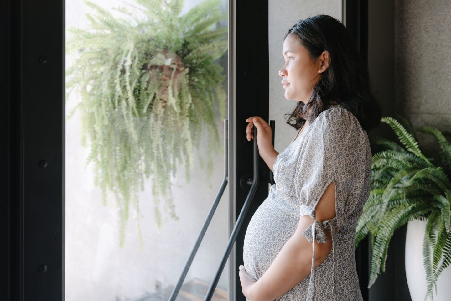 miscarriage anxiety: pregnant woman looking out window holding belly