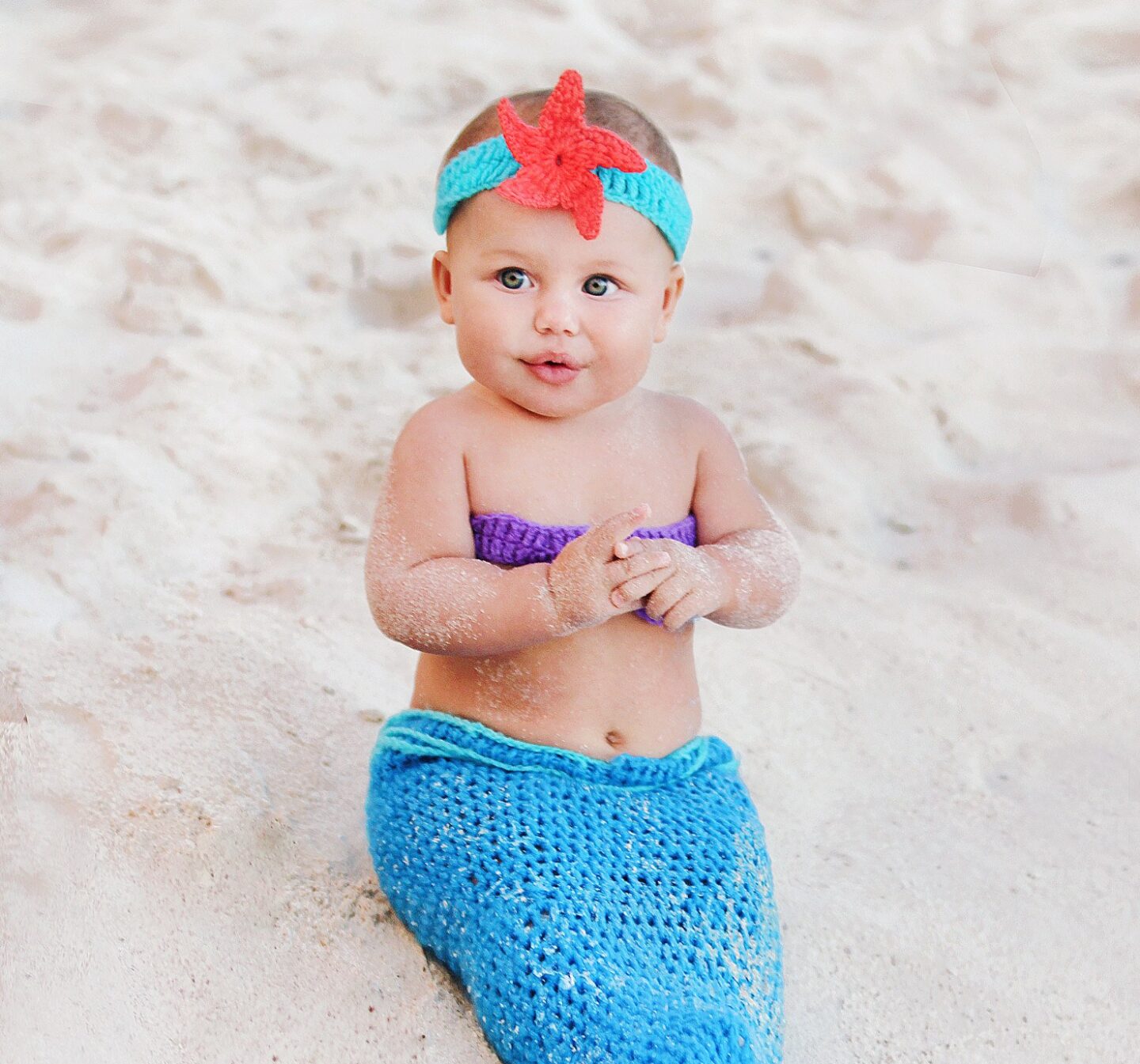 baby wearing a mermaid costume on a beach