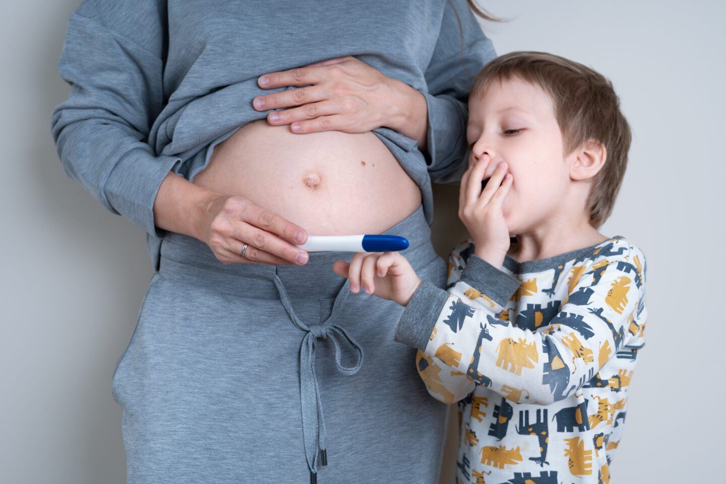 mom holding a pregnant mother holding pregnancy test with older son