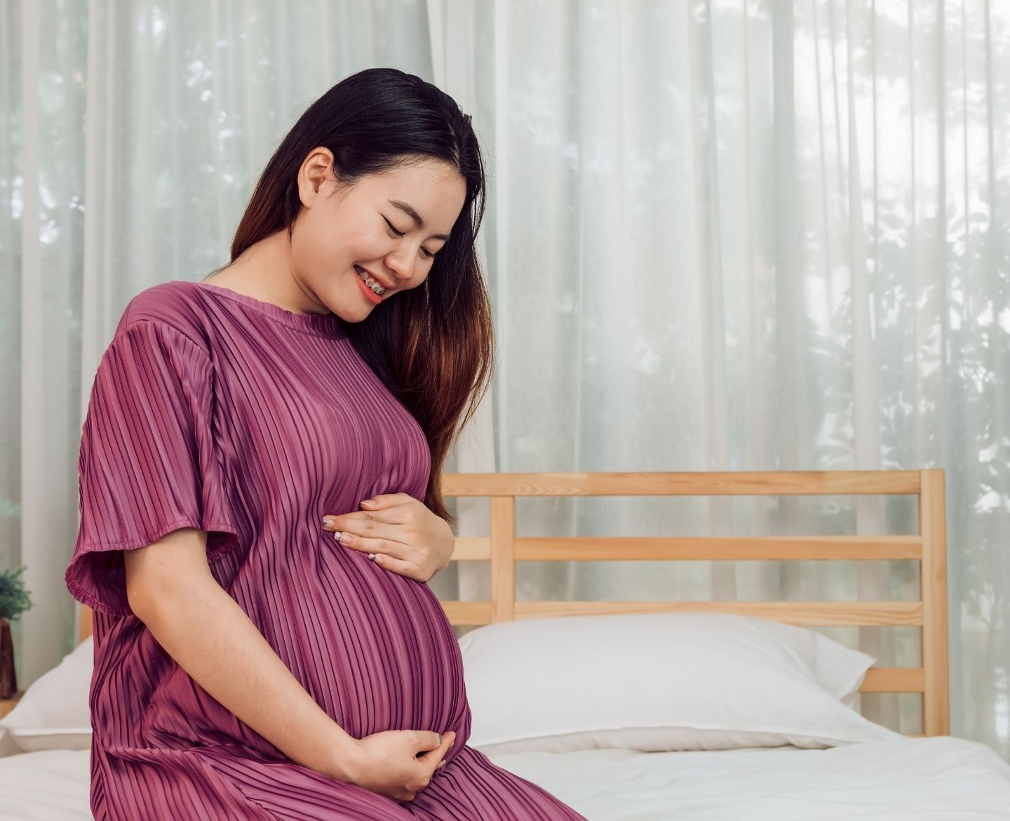 pregnant woman holding belly sitting on bed at home