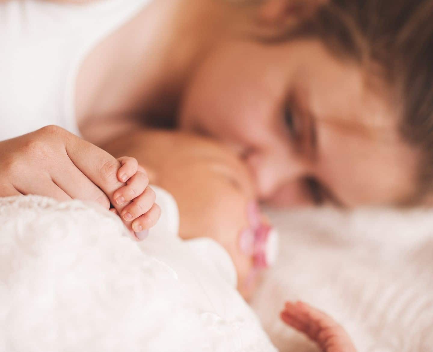 raising a child with a rare disease: sad woman lying on bed with baby