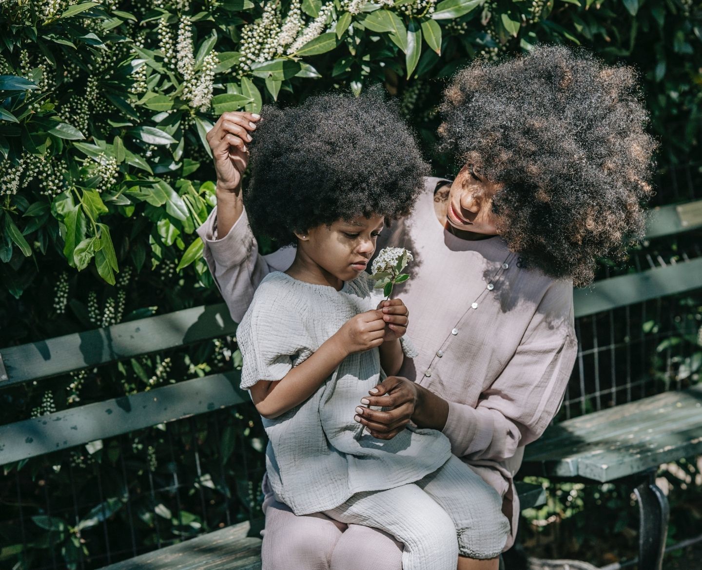 mother and child smelling a flower on a park bench