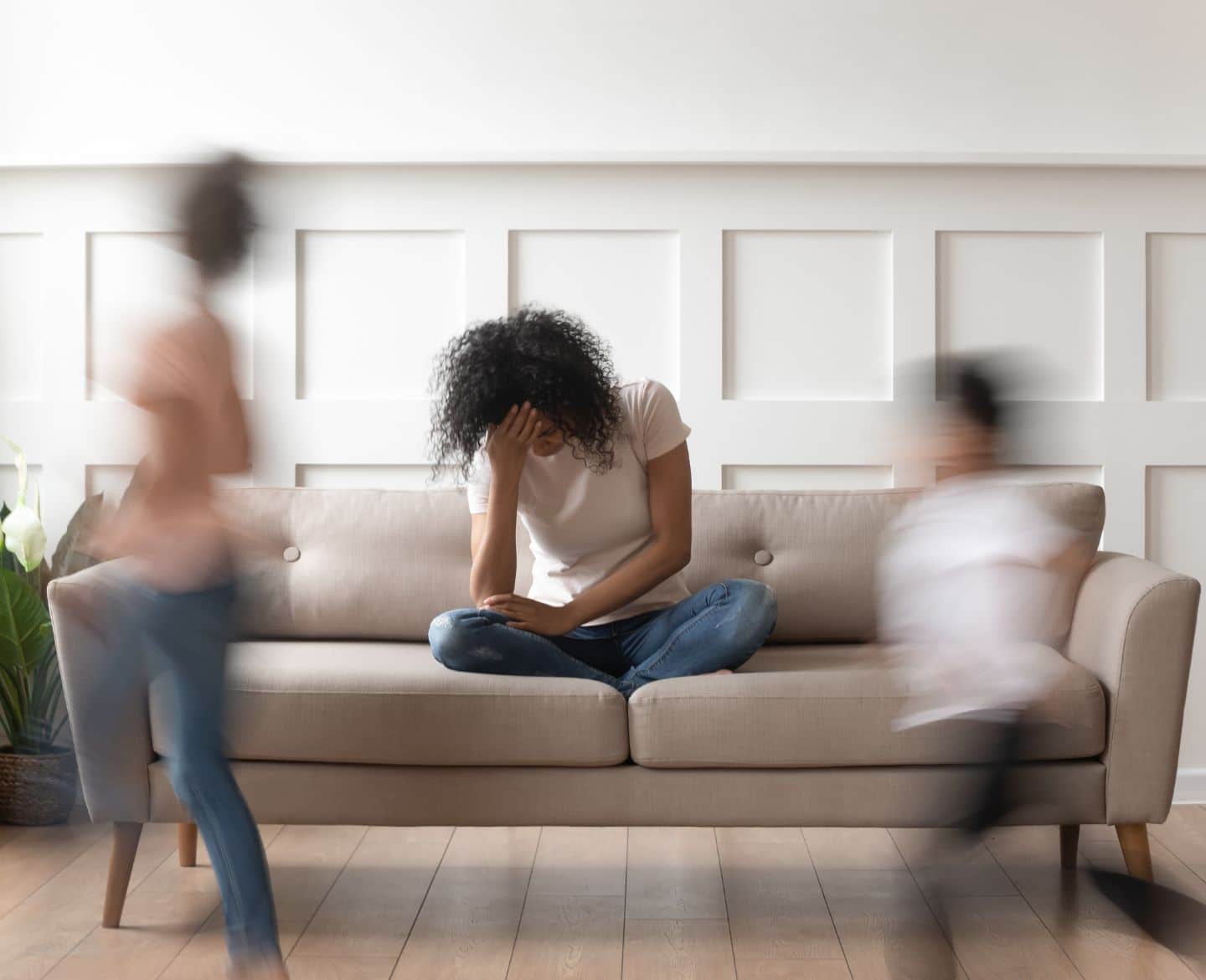 overwhelmed mom sitting on couch with kids running around