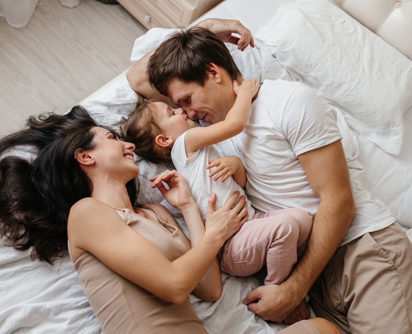 mother, father and daughter laying on bed smiling