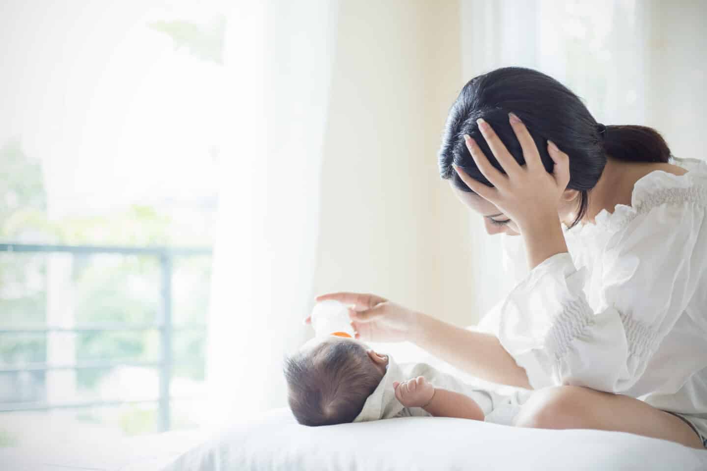 woman feeding baby a bottle on a bed